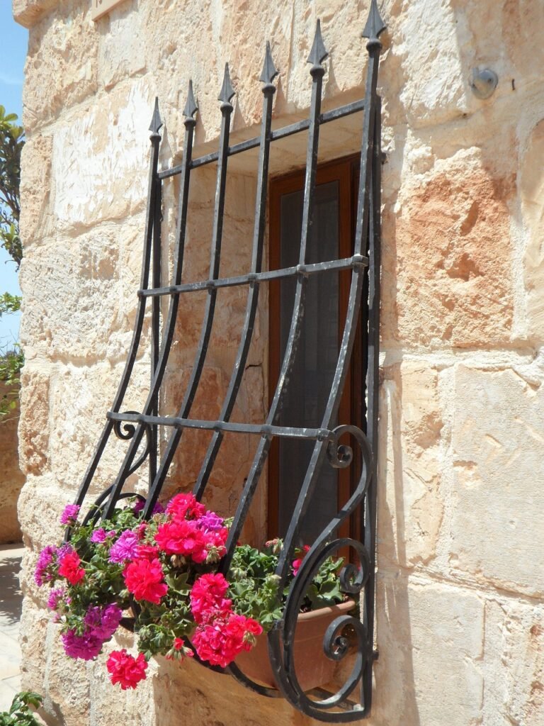 A decorative wrought iron window bar with flowers on the sill.