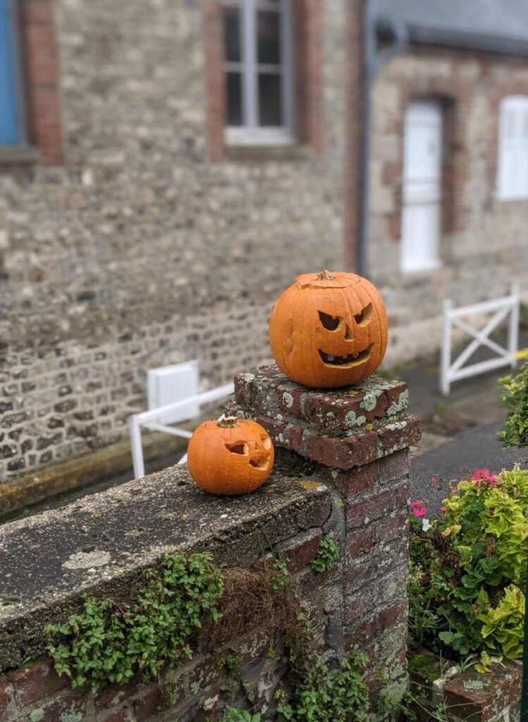 Festive Halloween pumpkins sit on a rustic brick wall in Veules-les-Roses, France.