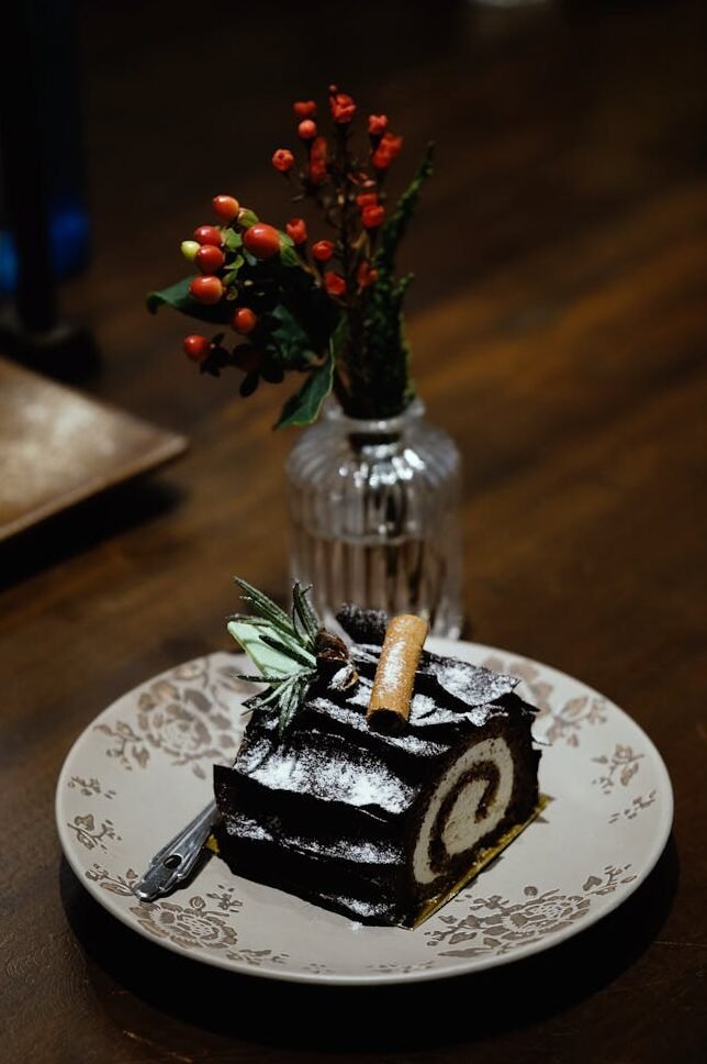 Chocolate yule log cake with powdered sugar and festive decorations on a plate.