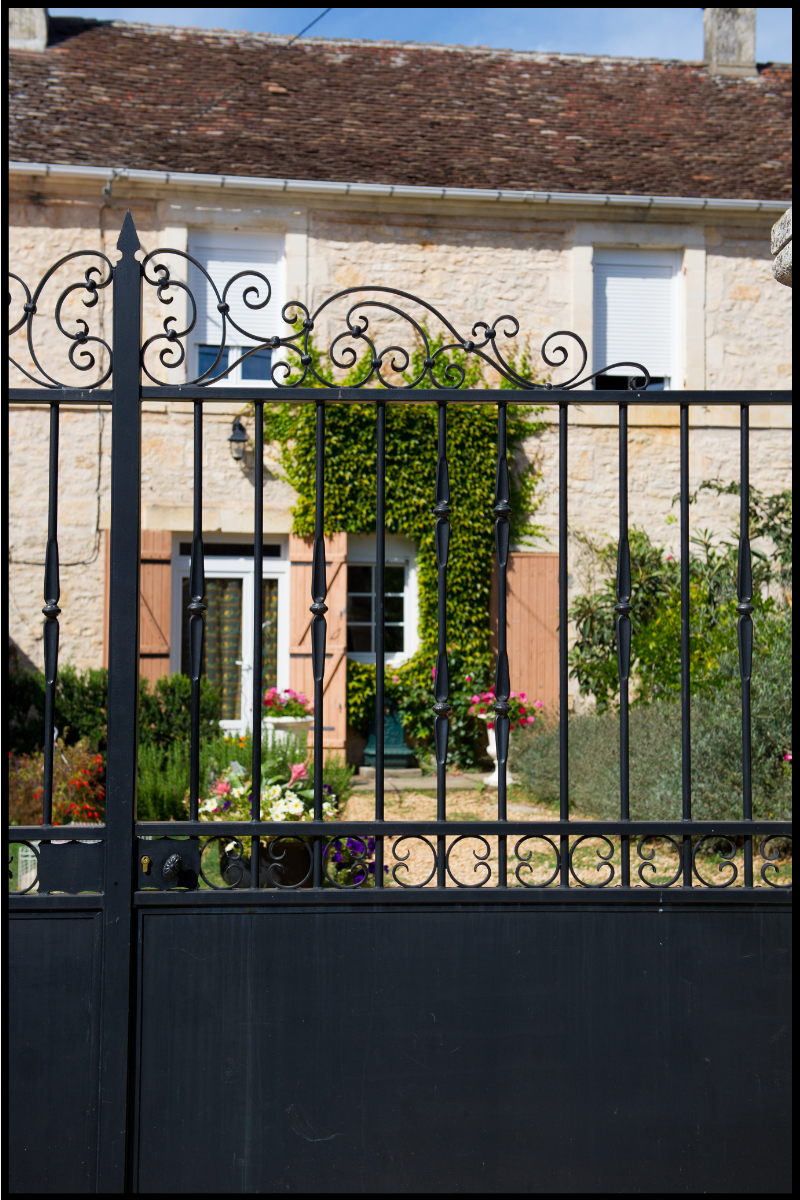 A stone house and garden behind a large iron gate