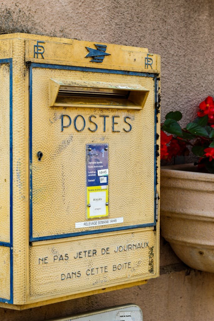 A classic yellow postal box on a street in France, with vibrant flowers nearby.