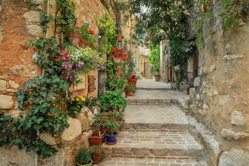 Beautiful cobblestone alley in France adorned with colorful flowers and stone architecture.