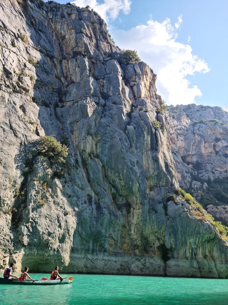 Three people canoe along the turquoise waters of Verdon Gorge, flanked by dramatic cliffs in Provence, France.