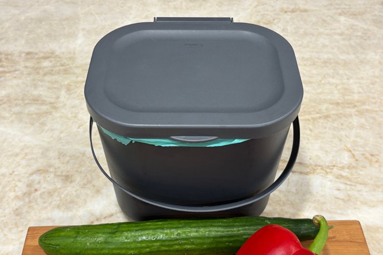 A tabletop compost bin near vegetables